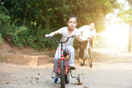 Portrait of active multi generations Asian family at nature park. Grandmother and granddaughter cycling outdoor. Morning sun flare background.の写真素材