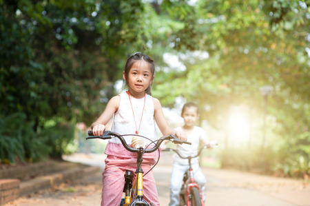 Portrait of active Asian family at nature park. Children riding bicycle outdoors. Morning sun flare background.の写真素材