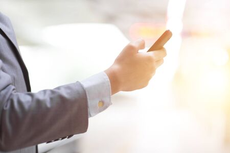 Business people using smart phone outdoors, focus on hand, bright sun flare background.の写真素材