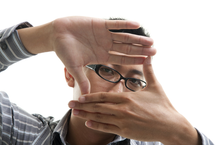Businessman making a frame with his hands, focus on his eyes, isolated on white background.の写真素材