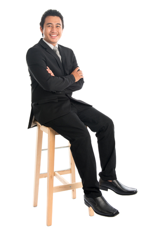 Full body portrait of handsome young Southeast Asian businessman sitting on high chair, isolated on white background. の写真素材