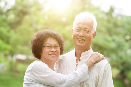 Happy Asian mature couple smiling in a park on a sunny day.の写真素材