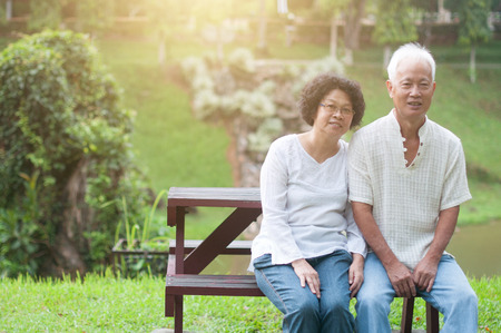 Happy Asian elderly couple sitting on bench in summer park.の写真素材