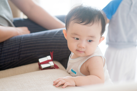 Nine months old baby boy holding sofa and learning how to walk. Asian family at home, living lifestyle indoors.の写真素材