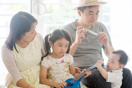 Parents and children singing and playing ukulele and harmonica together. Asian family spending quality time at home, living lifestyle indoors.の写真素材