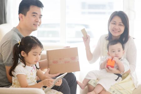 Online shopping using digital tablet pc and payment with credit card. Happy Asian family at home, natural living lifestyle indoors.の写真素材