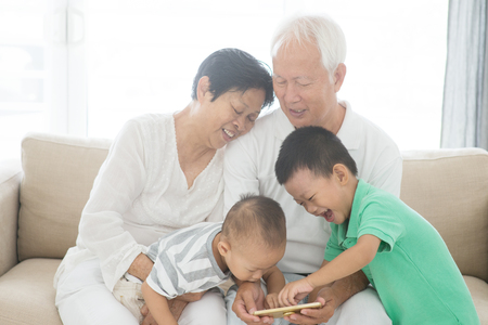 Portrait of happy Asian grandparents and grandchildren using smart phone at home, family indoor lifestyle.の写真素材