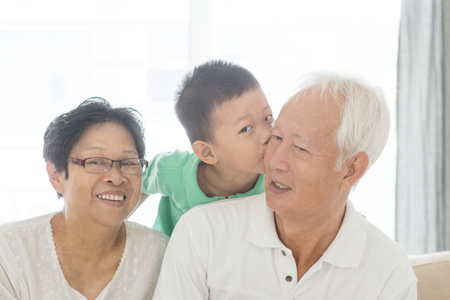 Portrait of happy Asian grandchild kissing grandparents at home, old senior retired people and child indoor lifestyle.の写真素材