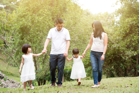 Asian family outdoors. Parents and children holding hands and walking at garden park.の写真素材