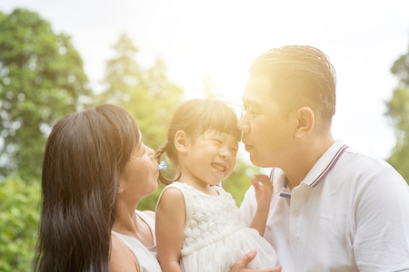 Parents kissing child at green park. Asian family outdoors activity.の写真素材