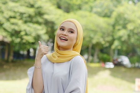 Portrait of cheerful Muslim girl thumb up, smiling at outdoor.