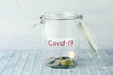 Coins in glass money jar with covid19 label, financial concept.の写真素材