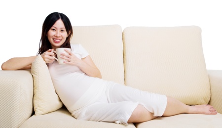 Pregnant woman rest on sofa, holding a cup of drinksの写真素材