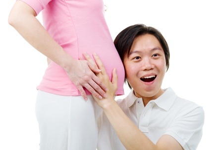 cheerful asian man listening to his pregnant wife bellyの写真素材