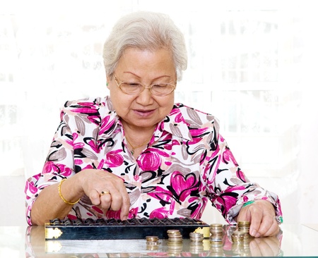 Asian senior woman using abacus to count coinsの写真素材