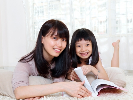 Asian woman and daughter lying on the floor and readingの写真素材