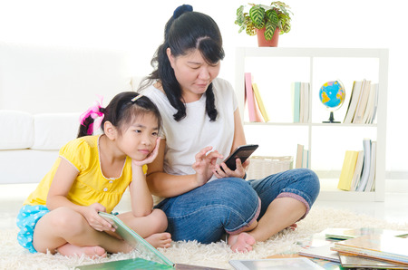 Asian child frustrated with her mother who is busy playing handphoneの写真素材