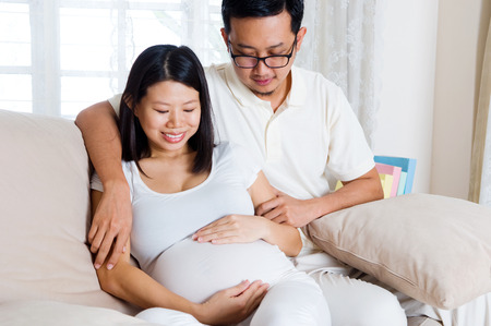 Asian man and his pregnant wife sitting on sofaの写真素材