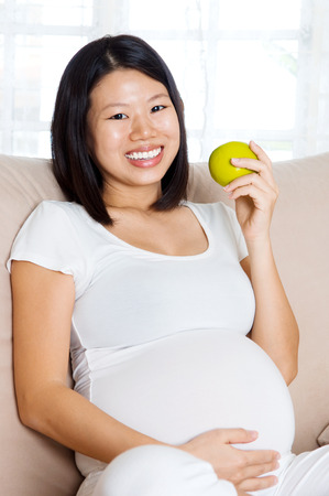 Asian pregnant woman eating an appleの写真素材