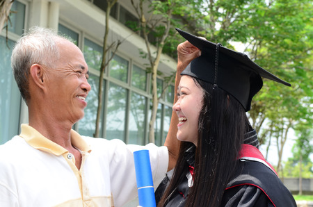 Asian man helping daughter to fix her mortarboard during graduationの写真素材
