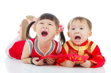 Asian kids in traditional chinese costume, cheongsam lying on the floor holding red packetの写真素材