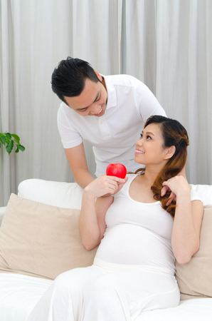 Asian man giving an apple to his pregnant wifeの写真素材