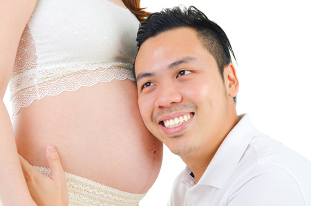 Asian man listening to his pregnant wife's stomachの写真素材