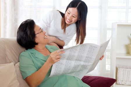 Asian senior woman holding newspaper and talking with daughterの写真素材