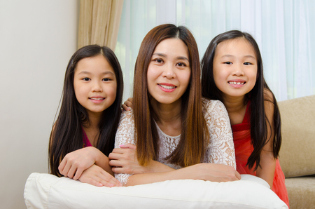 Indoor portrait of beautiful asian mother and daughters lying on sofaの写真素材