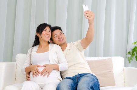 Asian pregnant woman and husband taking photo using handphoneの写真素材