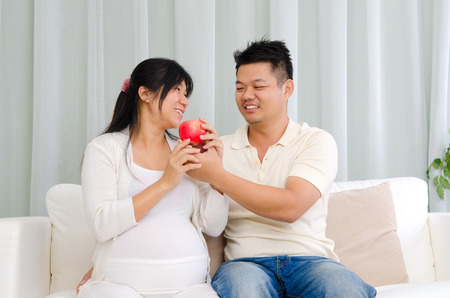 Asian man giving an apple to his pregnant wifeの写真素材