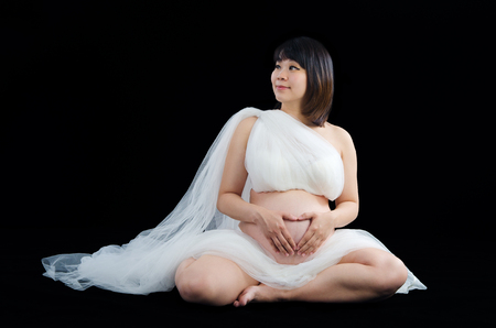 Asian pregnant woman making love shape with hands on ther stomachの写真素材