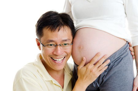 Asian man listening to his pregnant wife's stomachの写真素材
