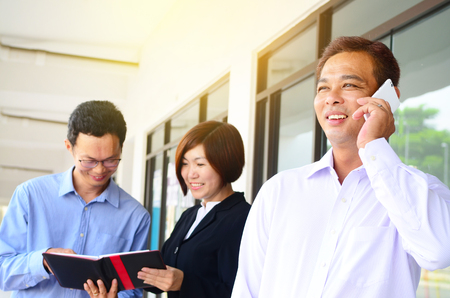 Asian middle aged businessman talking on the phone at workplaceの写真素材