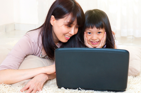 Asian mother and daughter using laptop at homeの写真素材