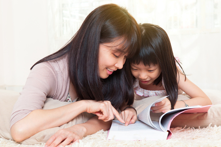 Asian mother and daughter reading a book togetherの写真素材