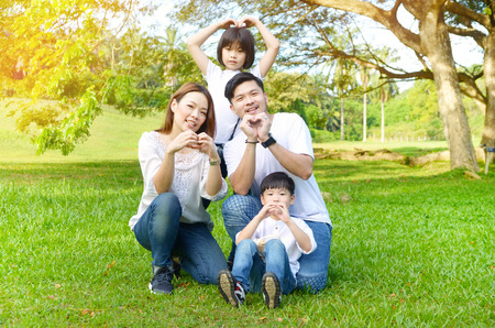 Outdoor portrait of beautiful asian family making love shape with handsの写真素材