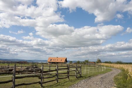 An idyllic landscape with fence, house and cloudy skyの写真素材