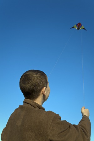 Boy flying a kite with clear blue skyの写真素材