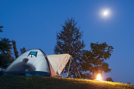 Camping in tent with human shadow and campfire, moon and stars on the clear blue skyの写真素材