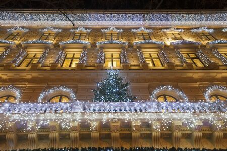 Building facade with light string decoration at night with Christmas tree on the balcony, door and large windowの写真素材