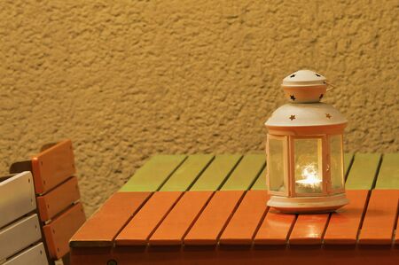 Small lighting candle lantern standing on colorful table before a wall