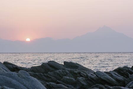 Early sunrise on rocky beach with high mountains in the distanceの写真素材