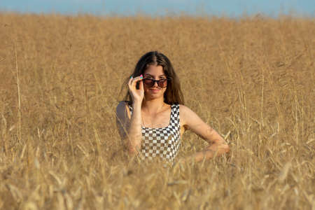 Young woman in sunglasses standing half-covered in wheat field on a sunny dayの写真素材