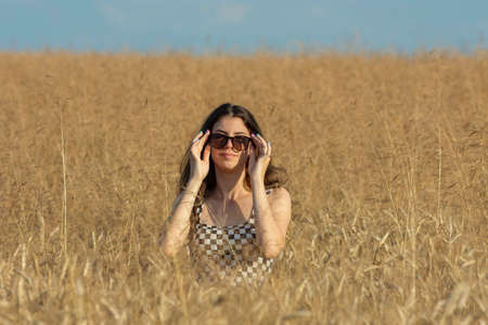 Young woman in sunglasses standing half-covered in wheat field on a sunny dayの写真素材