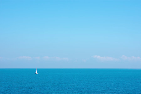 Tiny sailboat in the distance on the empty sea with empty sky and tiny cloudsの写真素材