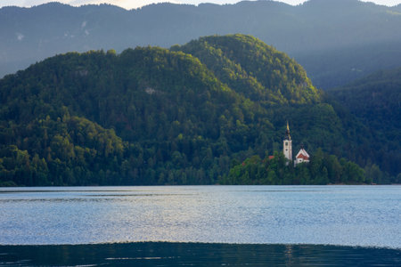 A small island with a church and green trees in a lake surrounded by high mountains, Bled, Sloveniaの写真素材