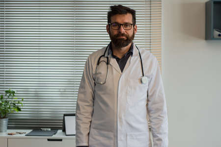 Close up portrait of handsome Caucasian senior joyful male doctor infectionist in white coat sitting...