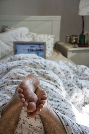 Man in bed with laptop focus on feet