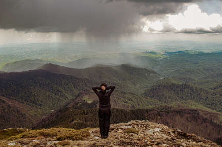 Rear view of a woman standing against the storm in the mountains